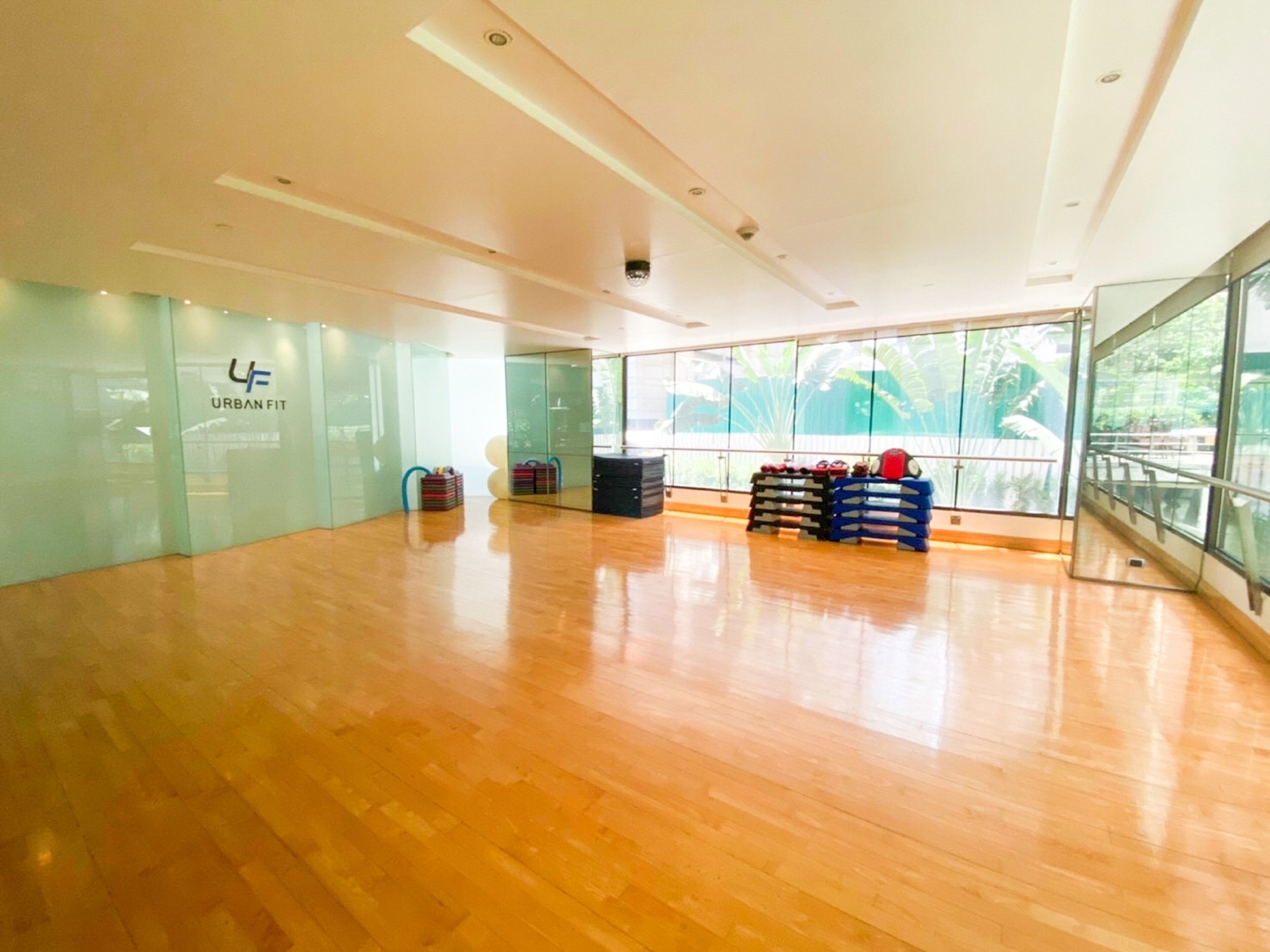 A spacious indoor area with a wooden floor, glass walls, and a large window offering a view of greenery outside.