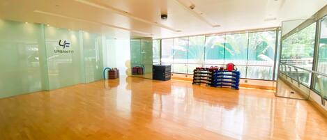 A spacious indoor area with a wooden floor, glass walls, and a large window offering a view of greenery outside.