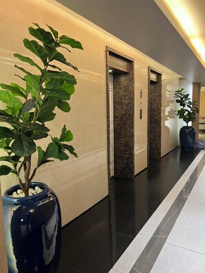 A modern hallway with marble walls, a black floor, and potted plants. - The Quarter Saladaeng by UHG  (Bangkok)