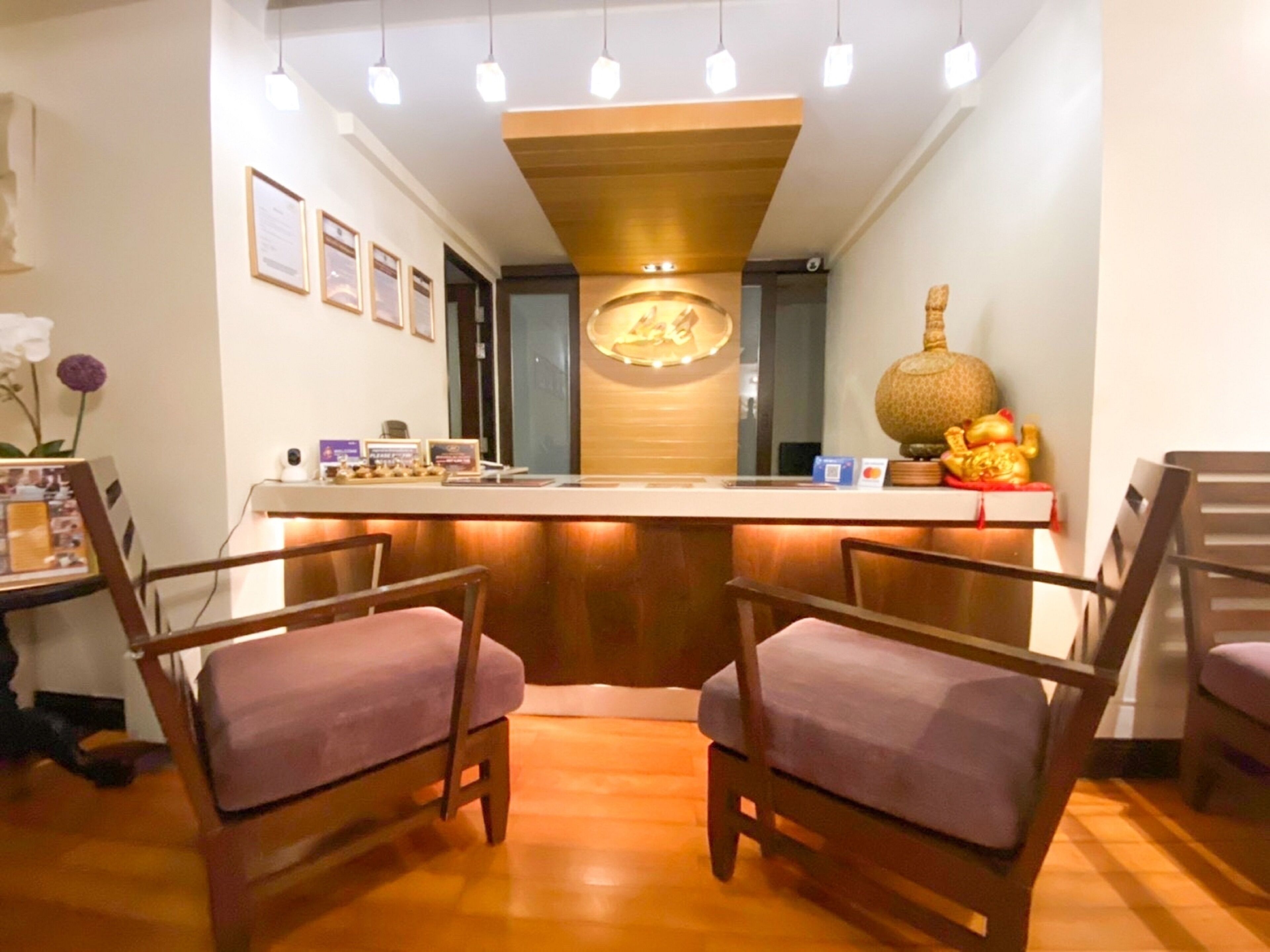 Un área de recepción con un mostrador de madera, dos sillas con cojines morados y un elemento decorativo en la pared.