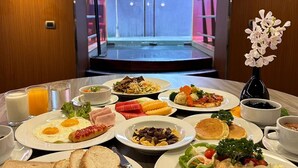 A breakfast buffet with various dishes, a vase of flowers, and a view of the hotel entrance.