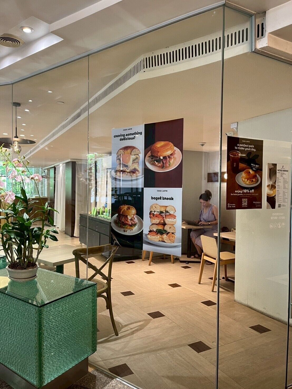Un interior moderno con un separador de vidrio, una planta en maceta y carteles promocionales de alimentos.