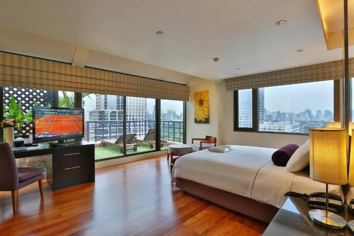 Habitación de hotel moderna con una cama grande, un escritorio con televisor y vistas a la ciudad a través de amplios ventanales.