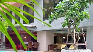 A swimming pool with a stone planter and a wooden structure, surrounded by a building with large windows and indoor seating.