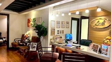 Una zona de recepción con un mostrador de madera, varias sillas, certificados enmarcados en la pared y una planta grande.