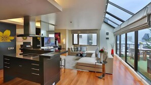 A modern living room with a large window, a kitchen area, and a sofa.