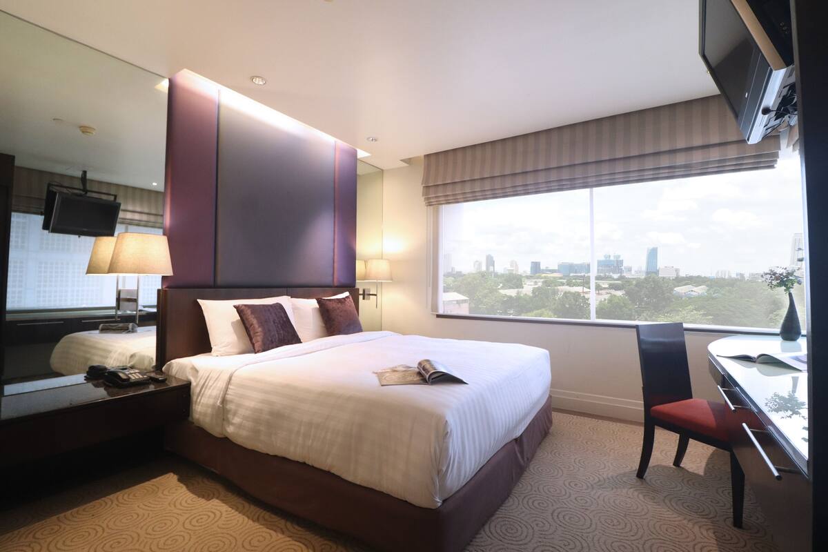 Un hotel moderno con una cama grande, un escritorio con silla, un televisor y vistas a la ciudad desde la ventana.