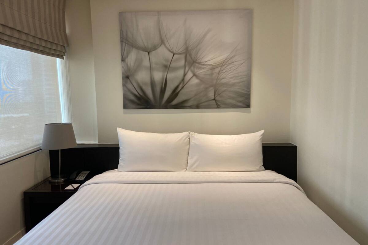 Una habitación de hotel con una cama grande, una mesita de noche con lámpara y teléfono, y una ventana con persianas.
