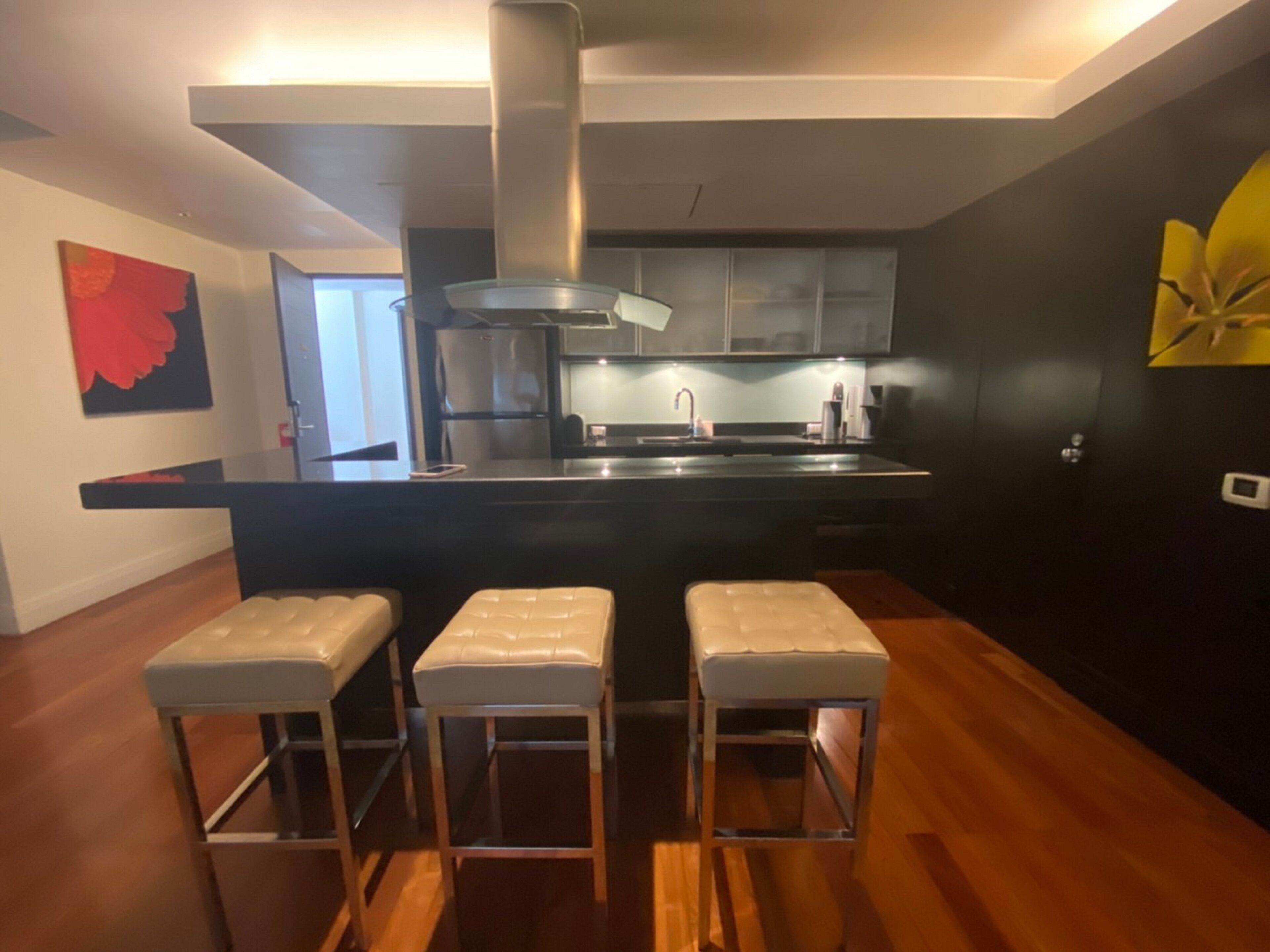 A modern kitchen with a central island, stainless steel appliances, and three bar stools.
