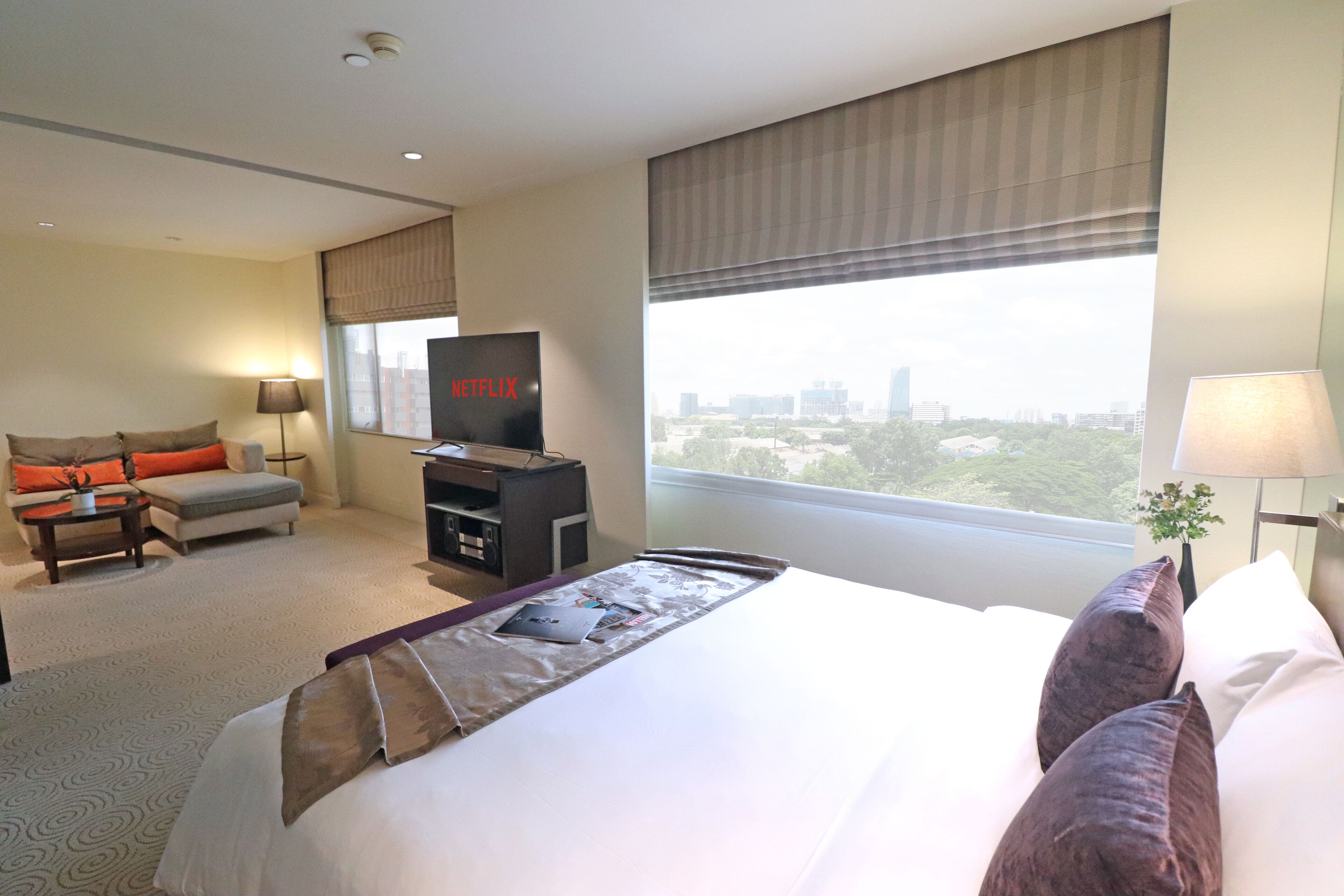 A hotel room with a large bed, a television, a desk, and a view of the city.