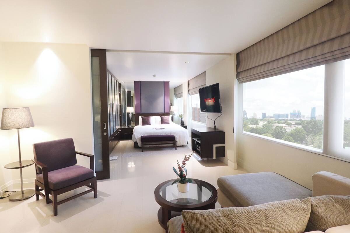 Una habitación de hotel moderna con cama, televisor, sofá, sillón y vistas a la ciudad.