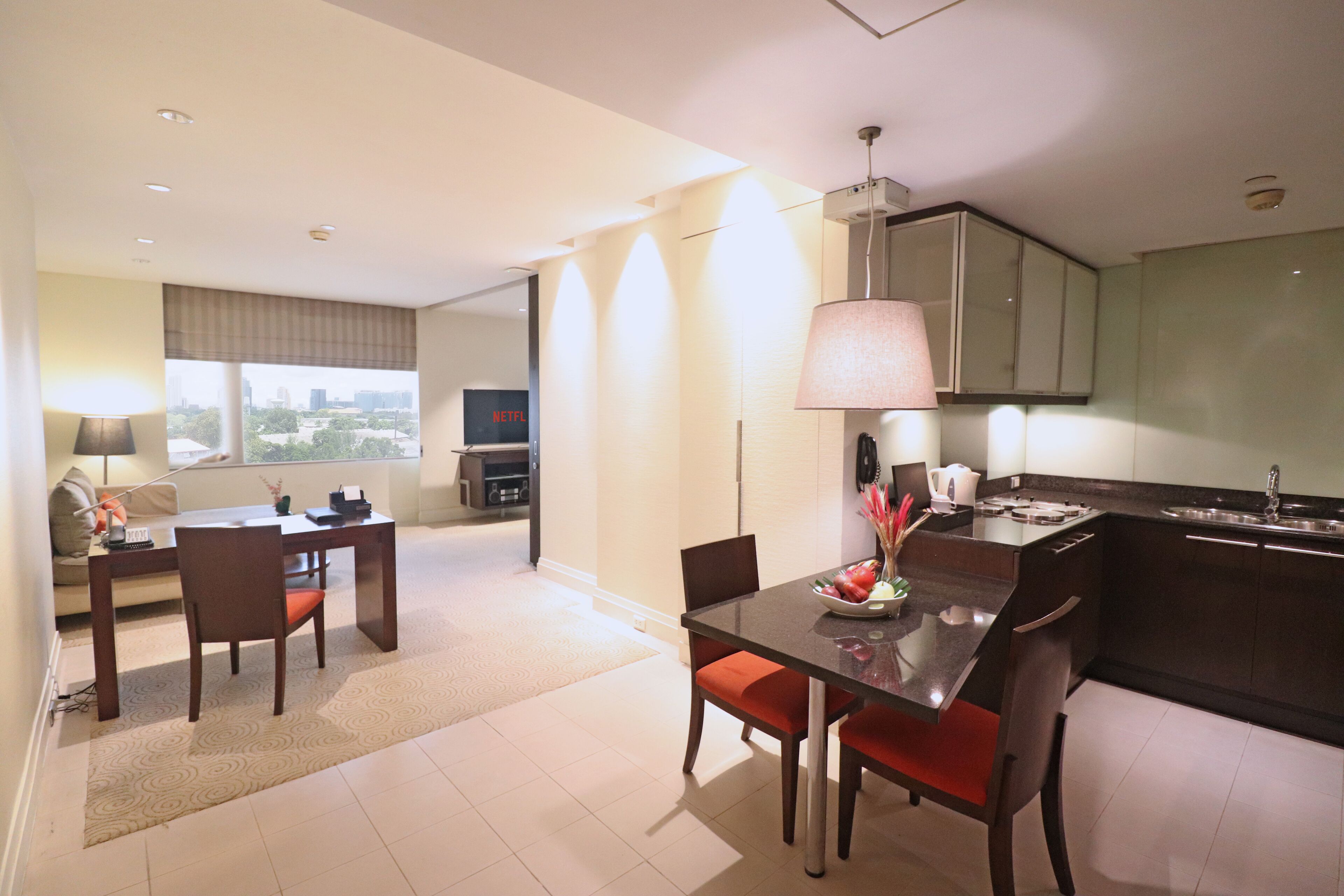 Una habitación de hotel moderna con zona de comedor, cocina y un amplio ventanal con vista a la ciudad.