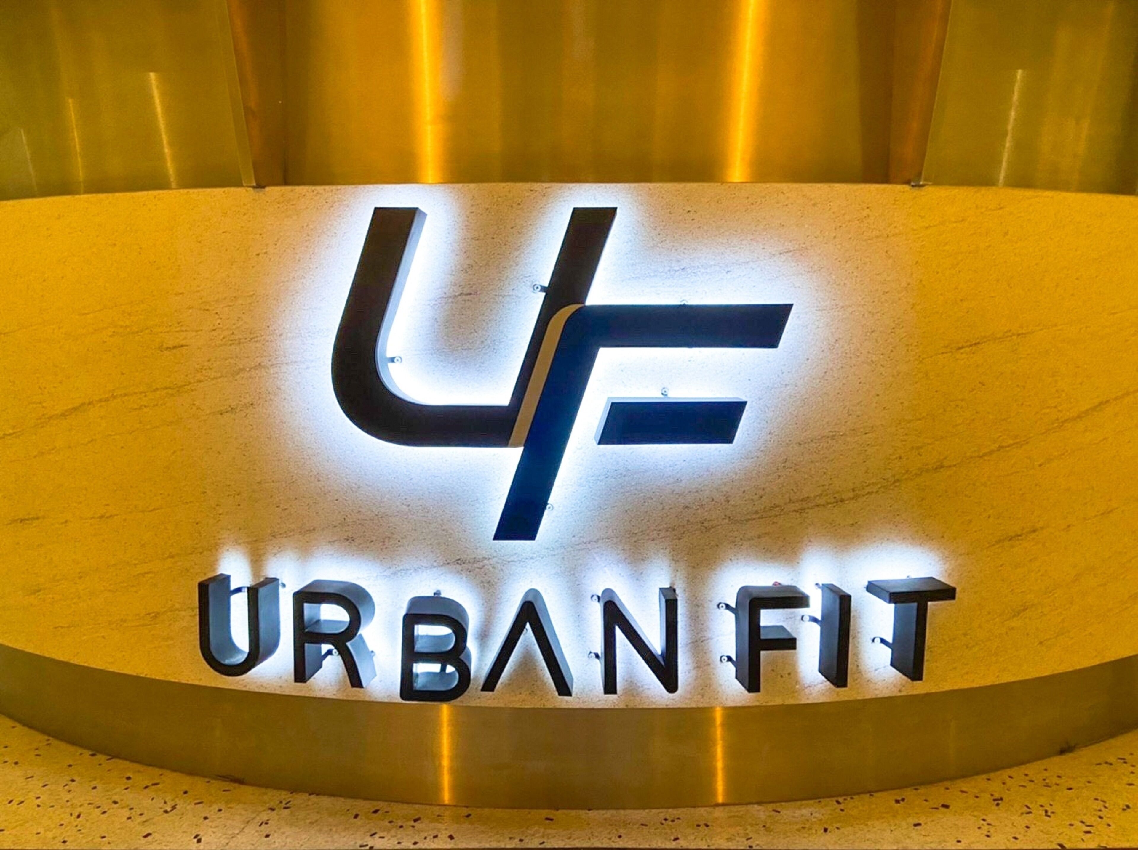A metallic sign with the letters "UF" and the words "URBAN FIT" in a modern, illuminated font.