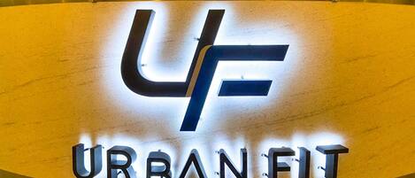 Un letrero metálico con las letras “UF” y las palabras “URBAN FIT” en una tipografía moderna e iluminada.
