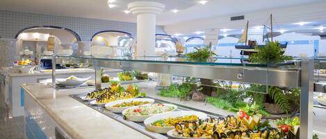 A buffet with various dishes, including seafood, arranged on a counter with a glass barrier.