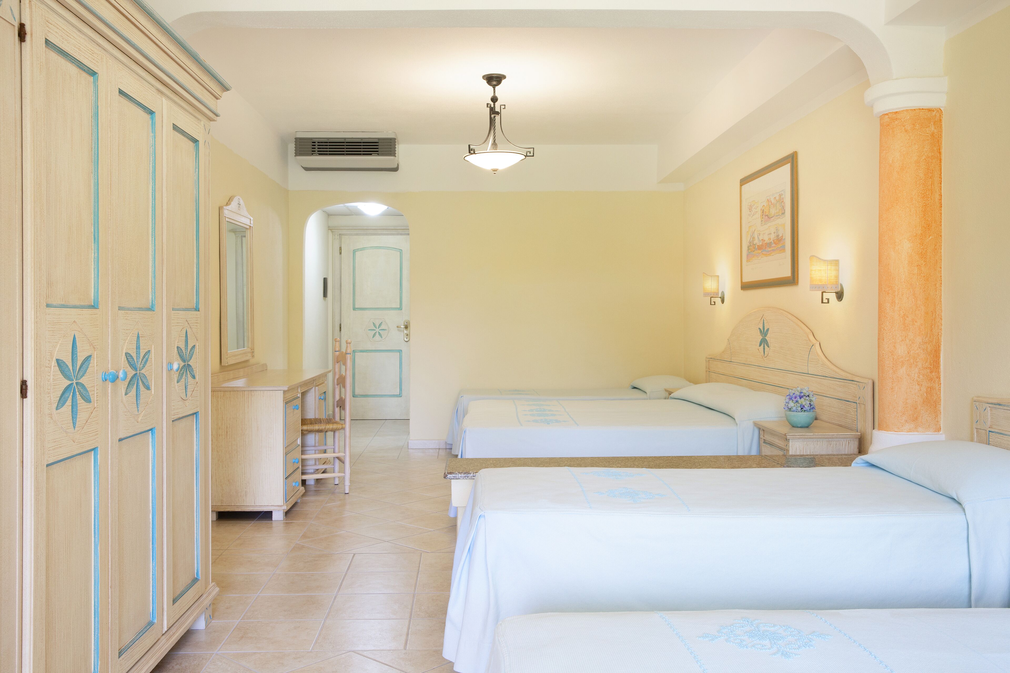 Habitación de hotel con dos camas, un armario, un espejo, un ventilador de techo y un cuadro en la pared.