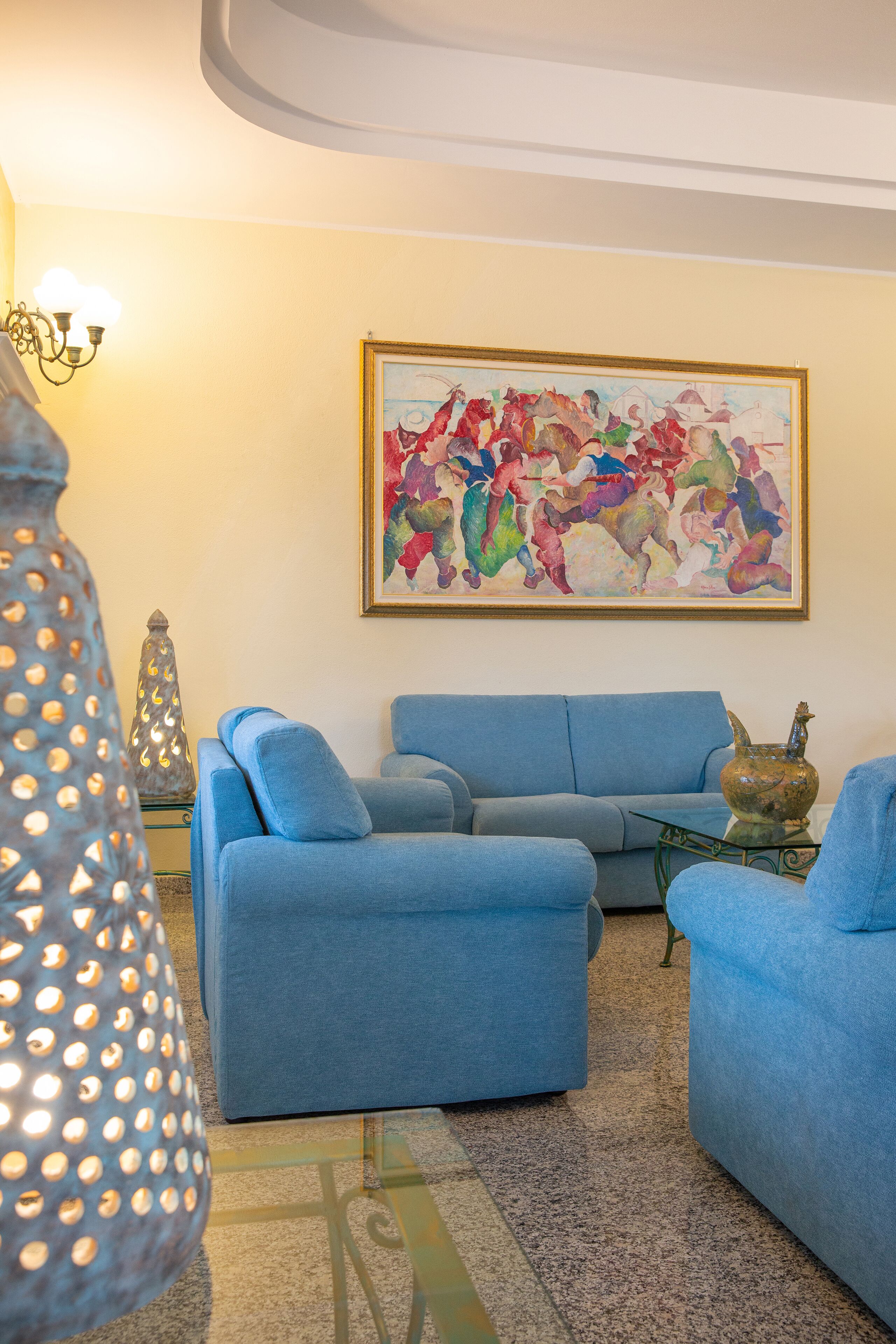 A living room with a blue sofa, a glass coffee table, and a colorful abstract painting on the wall.