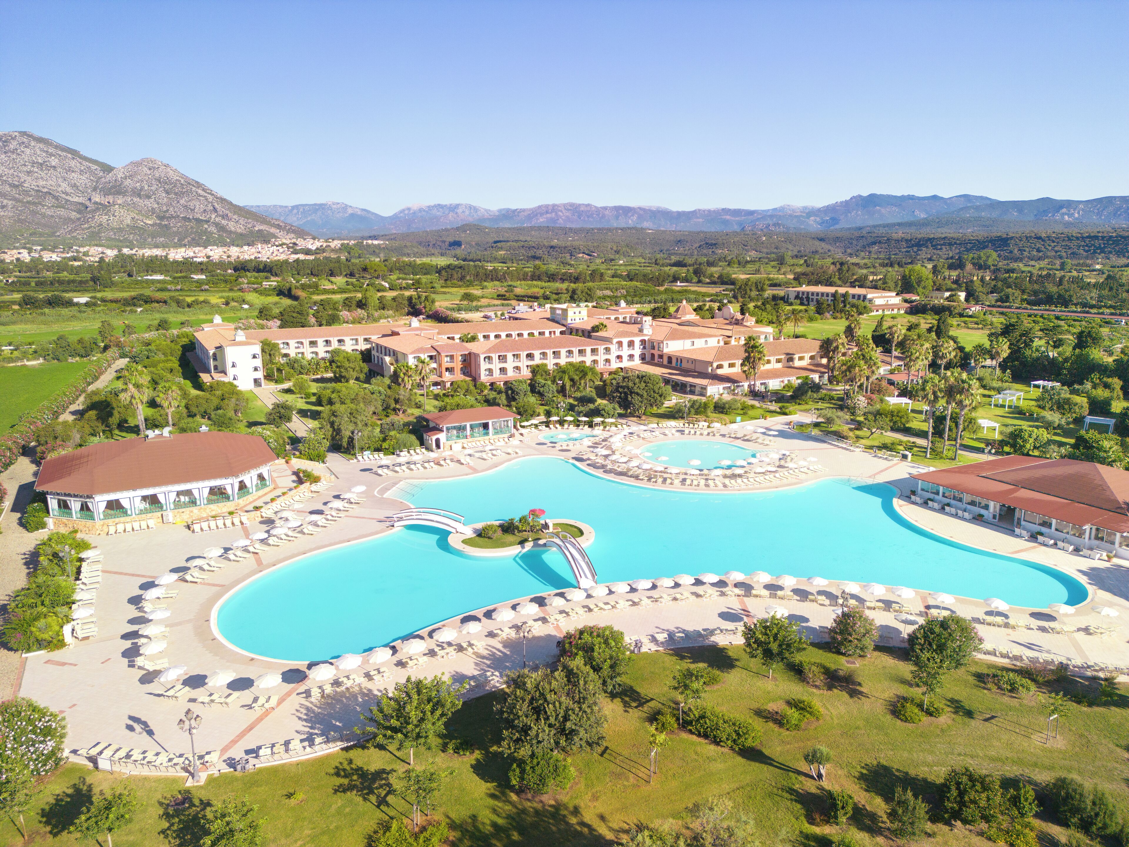 A resort with a large central pool, multiple buildings, and surrounding greenery.