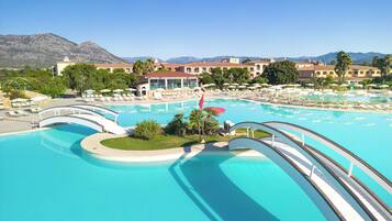 Una gran piscina con varios niveles y un puente, rodeada de sillas de descanso y sombrillas.