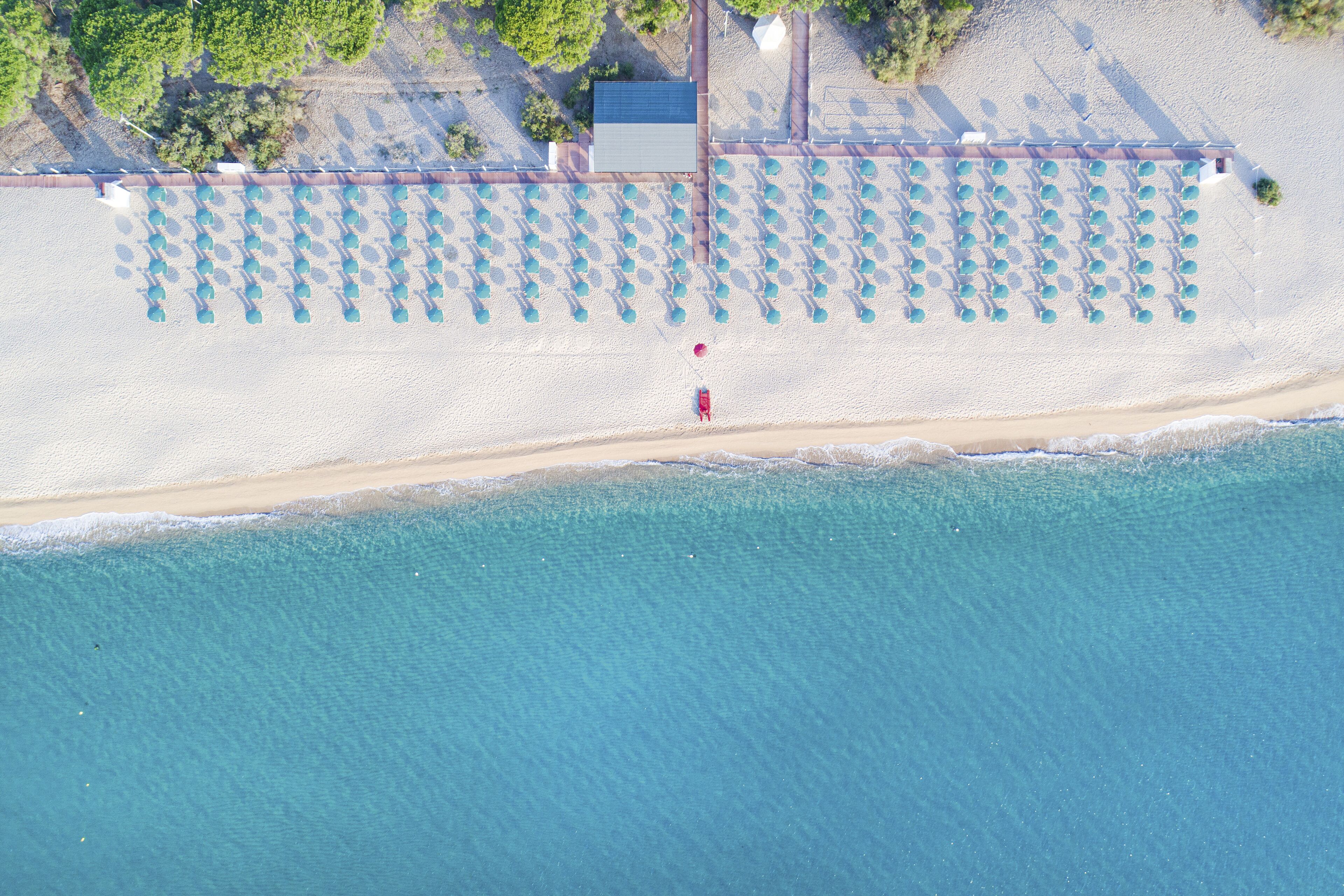An aerial view of a beach with rows of umbrellas and a building in the background.