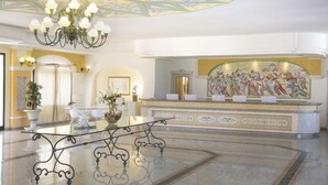 A lobby with a chandelier, a reception desk, a large mural, and a polished marble floor. - Club Hotel Marina Beach (Orosei)