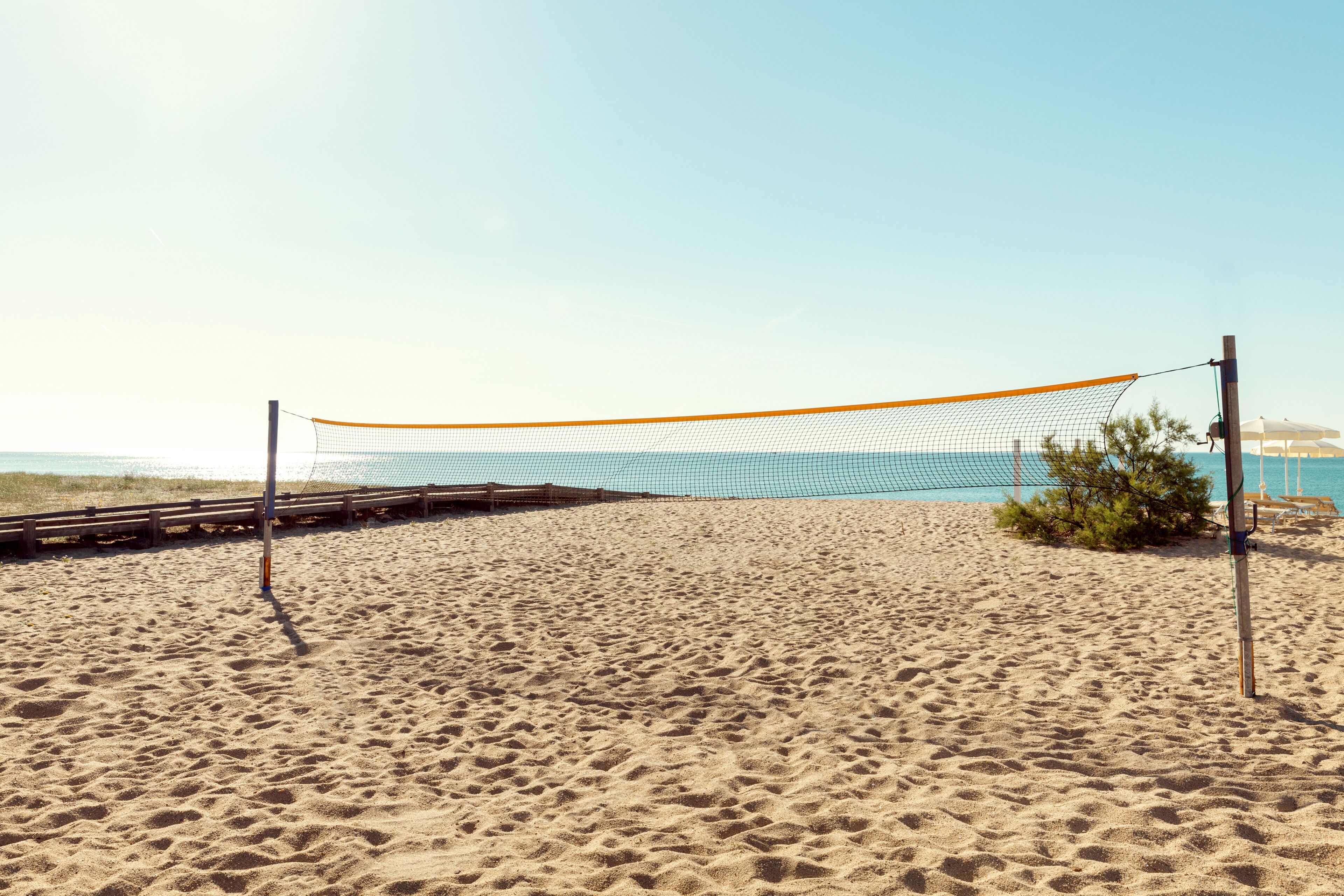 A beach volleyball net on a sandy beach with a clear sky.
