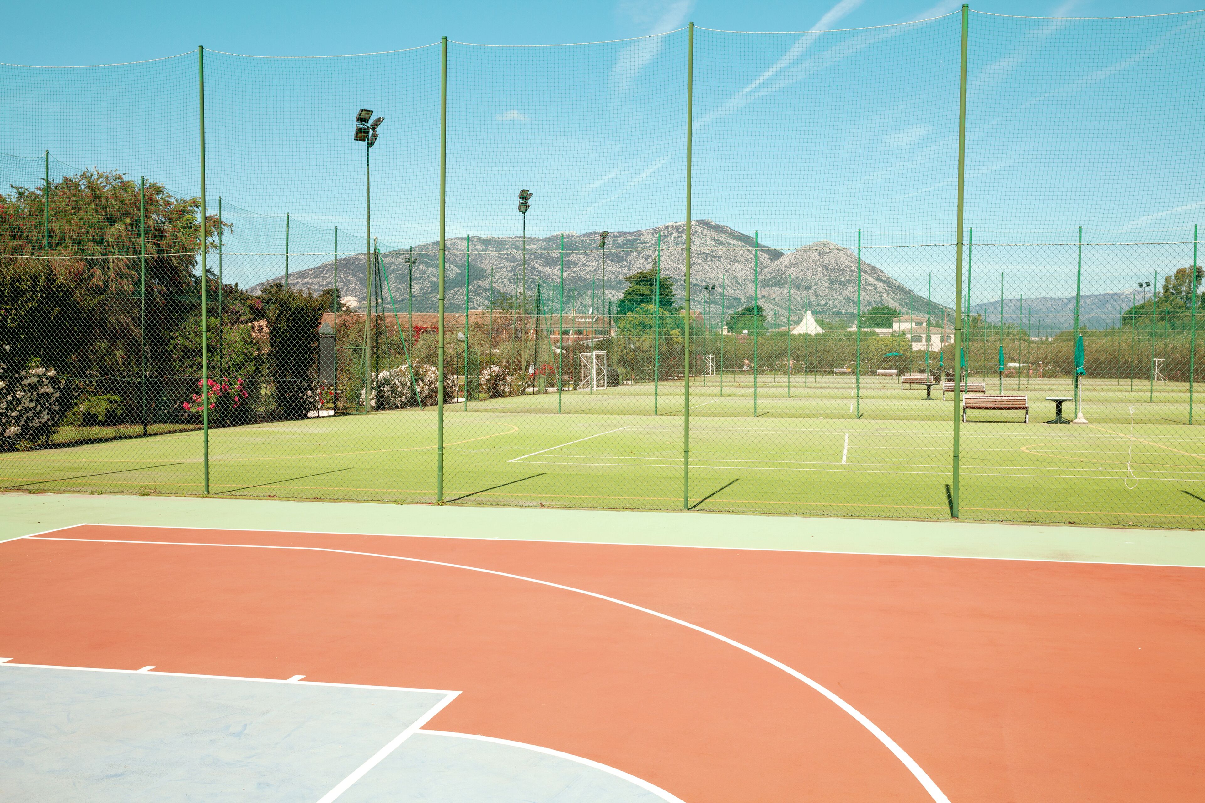 Ein Tennisplatz im Freien mit Netz, umgeben von einer Umzäunung, und ein Berg im Hintergrund.