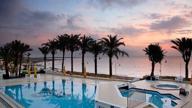 A pool area with palm trees, a view of the sea, and a sunset.