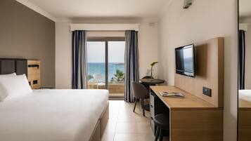 Habitación de hotel con cama, escritorio, televisor y vista al mar.