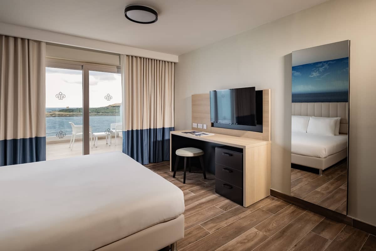 A hotel room with a bed, a desk, a chair, a TV, and a large window with curtains.
