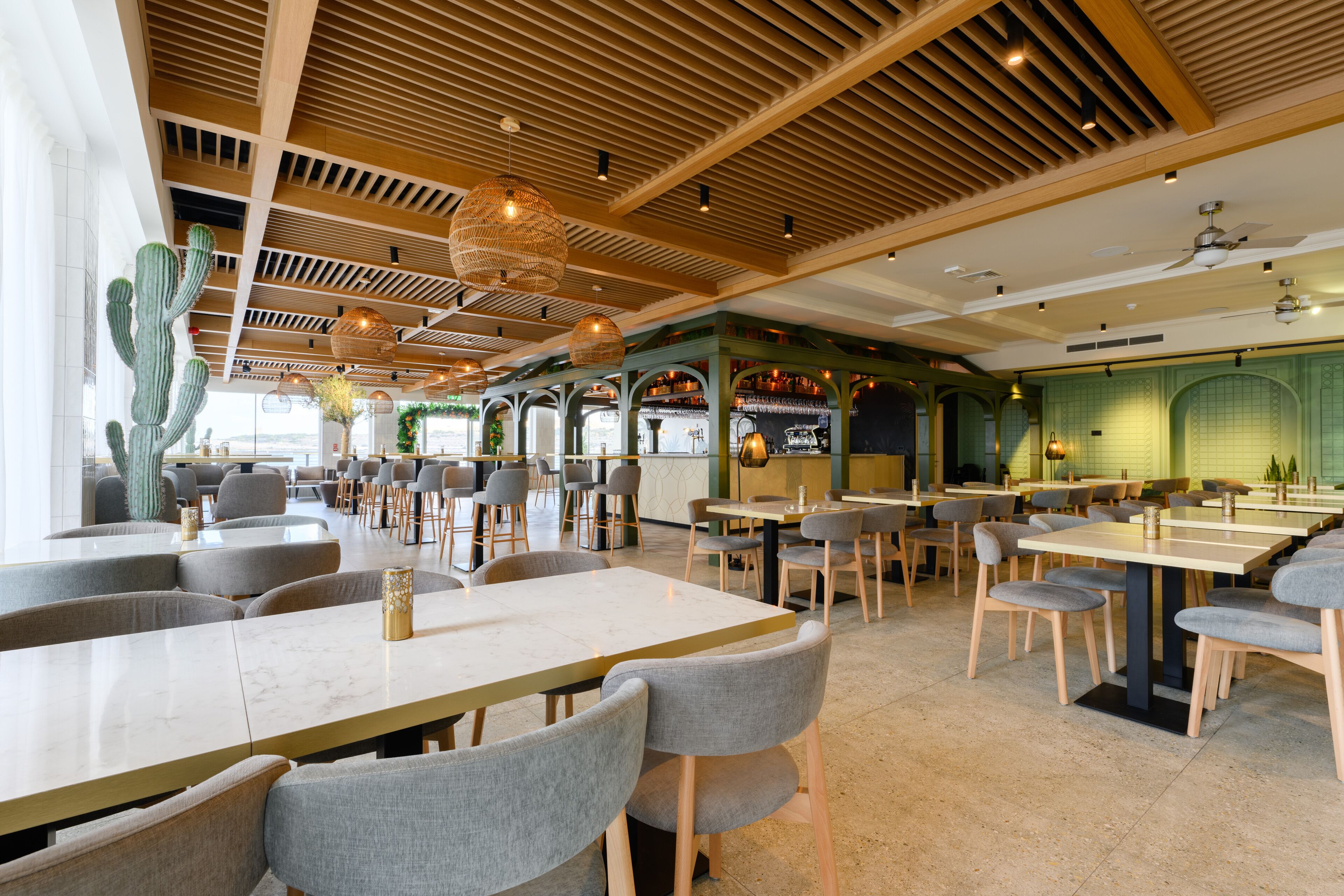 A spacious restaurant with high wooden ceilings, modern furniture, and a cactus decoration.