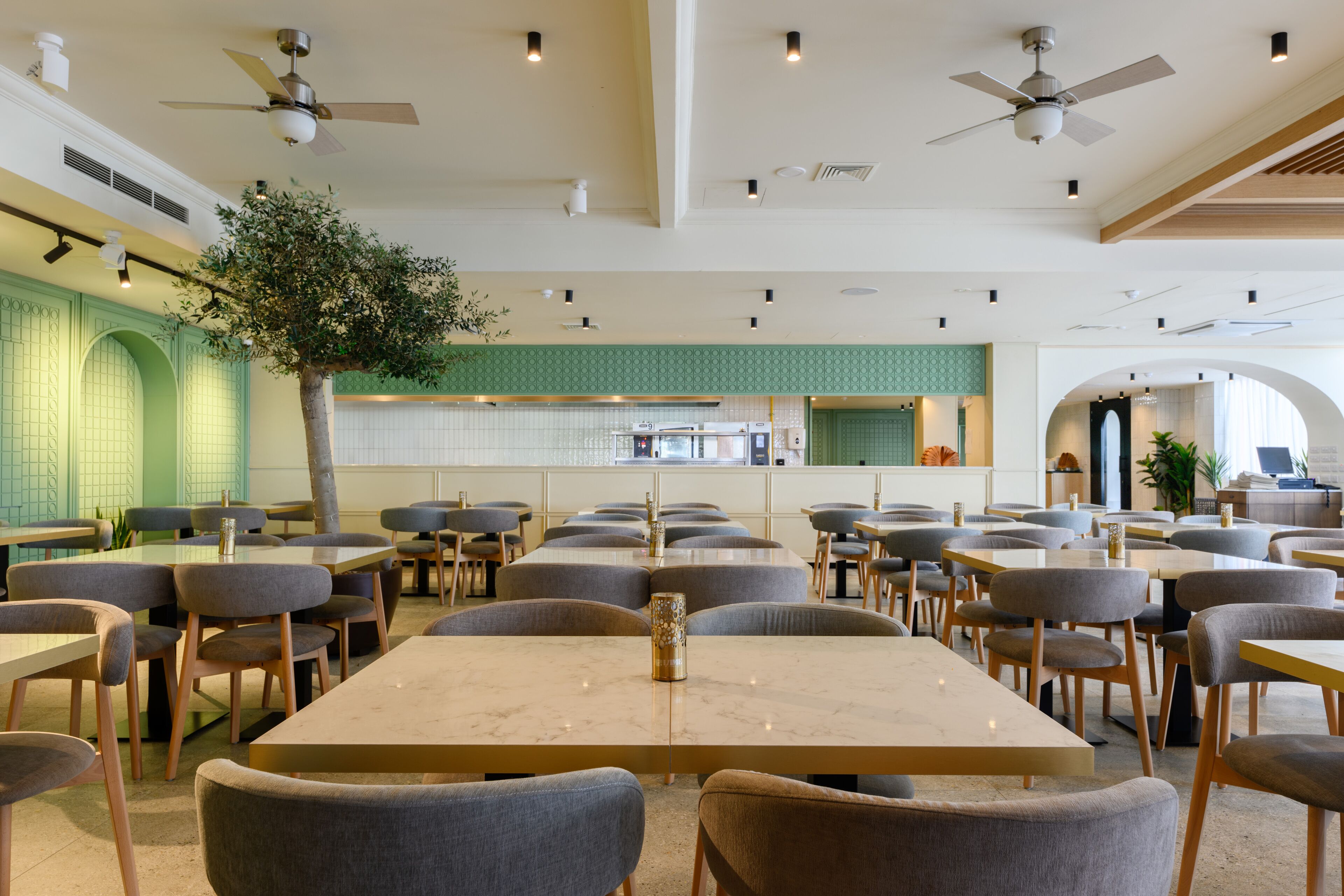 A spacious dining area with multiple tables and chairs, ceiling fans, and a central decorative tree.