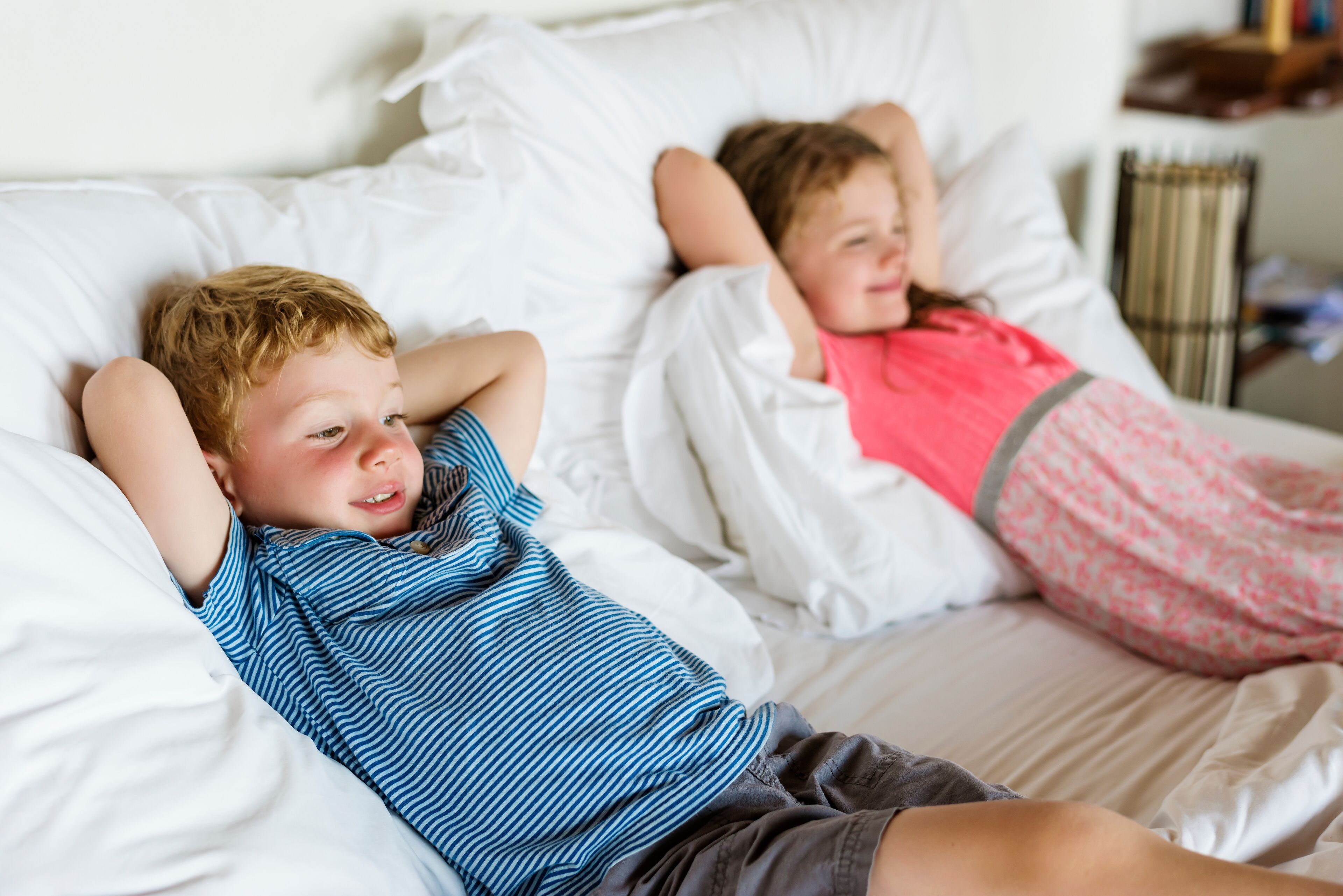 Two children lying in bed with white bedding.