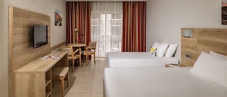 Habitación de hotel con dos camas, un escritorio con silla, televisor y ventana con cortinas.