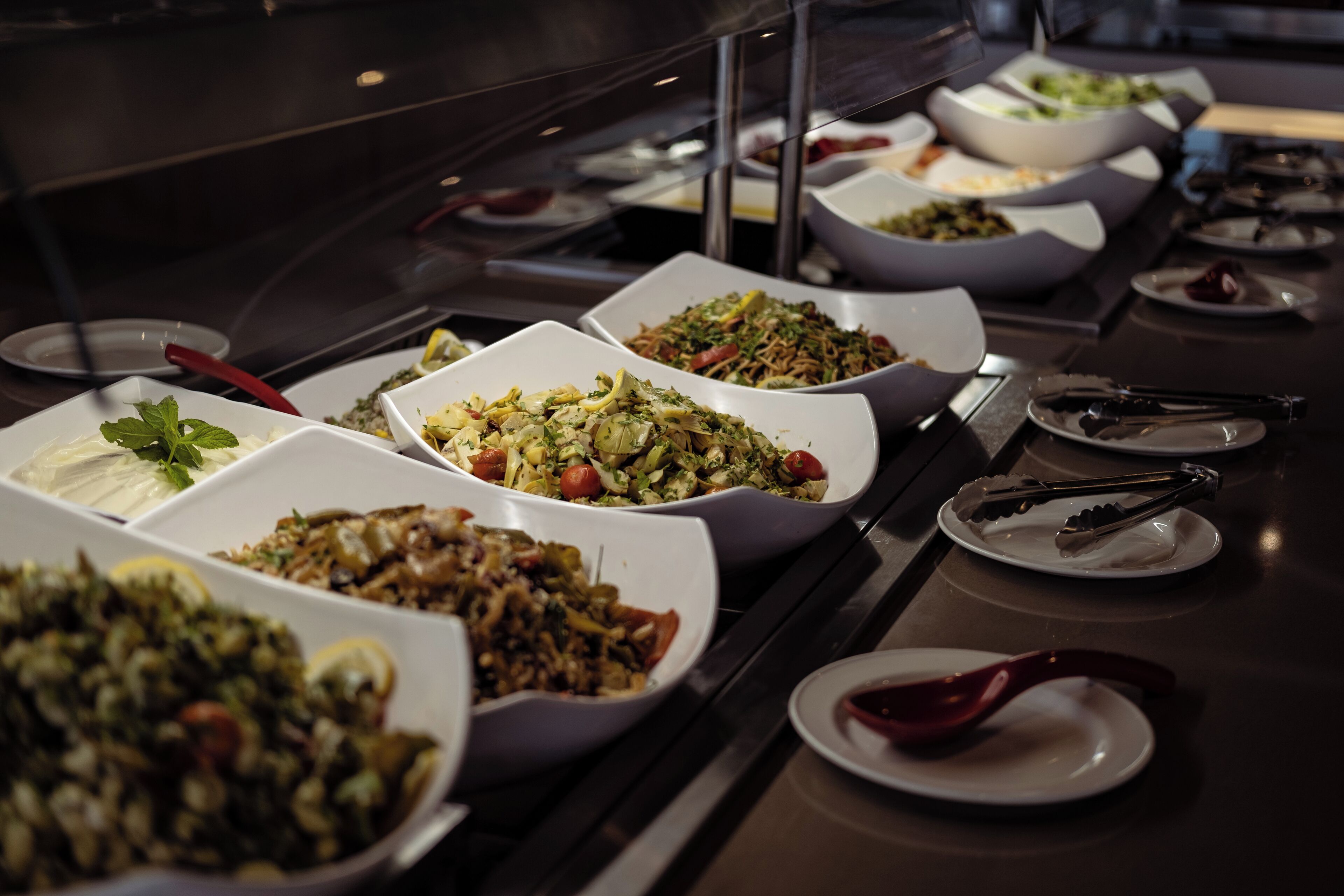 Een buffettafel met diverse gerechten in witte schalen, opgesteld in een rij.