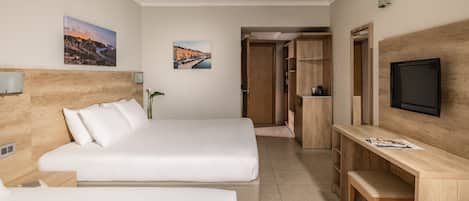 A hotel room with a bed, a desk, a television, and two wall-mounted pictures.