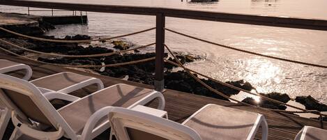 A deck with lounge chairs overlooking a calm sea with boats.