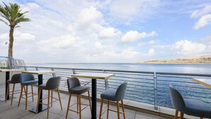 An outdoor seating area with tables and chairs, overlooking a body of water and a distant shoreline.