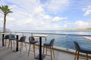 Un espace extérieur aménagé avec des tables et des chaises, offrant une vue sur une étendue d’eau et une côte lointaine.