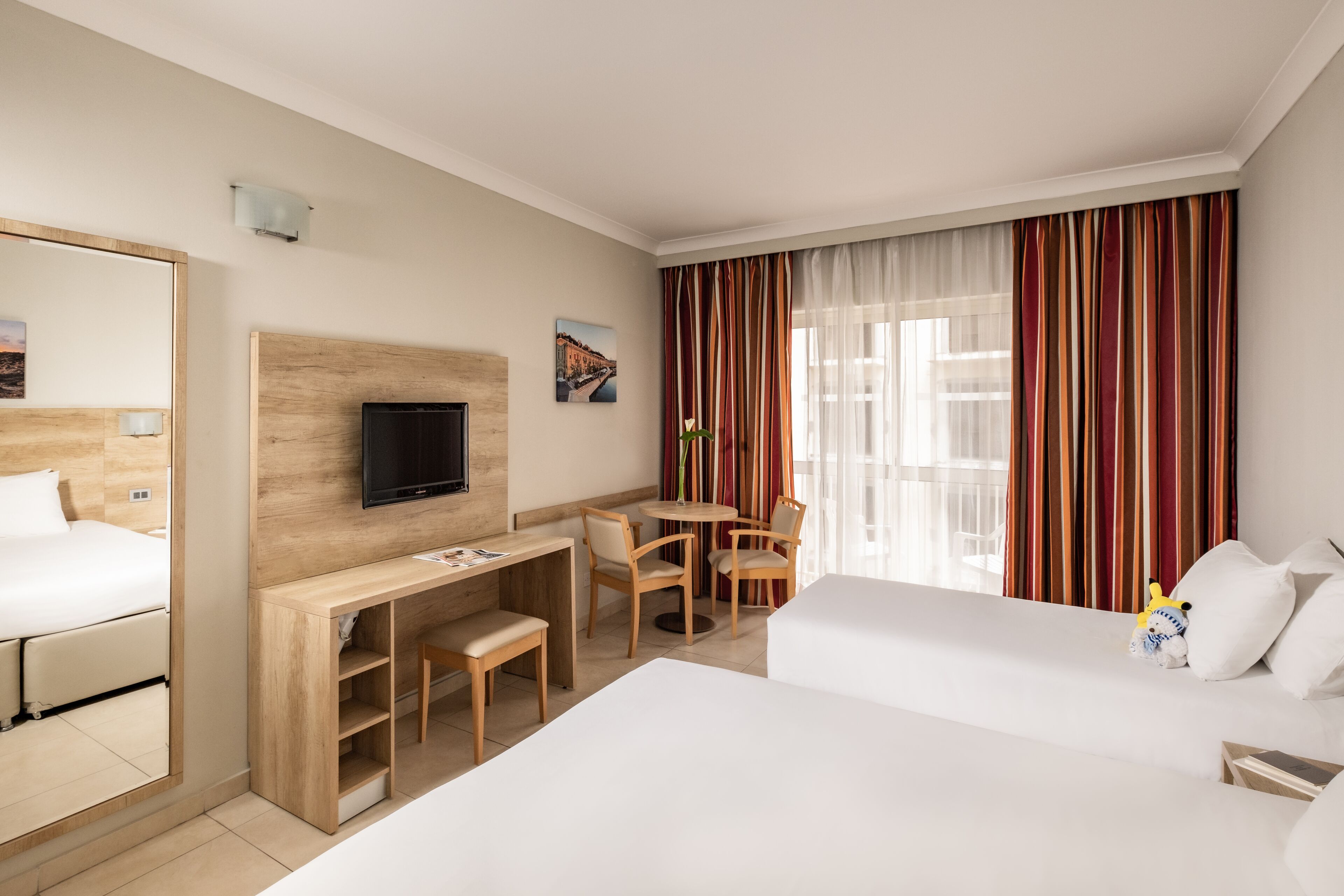 A hotel room with a bed, a desk with a chair, a television, and a window with curtains.