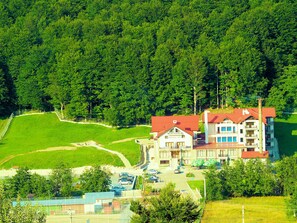 A multi-story hotel with a red roof, surrounded by lush greenery and a parking area.