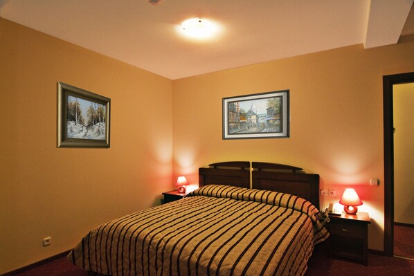 A hotel room with a bed, two bedside tables with lamps, and two framed pictures on the walls. - Hotel Floris (Maneciu)
