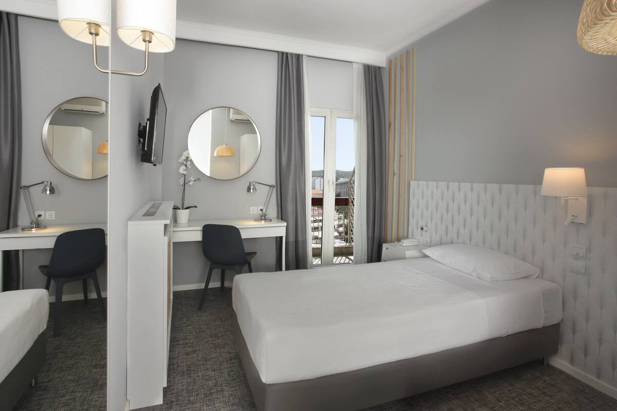 A hotel room with a bed, desk, chairs, and a large window.