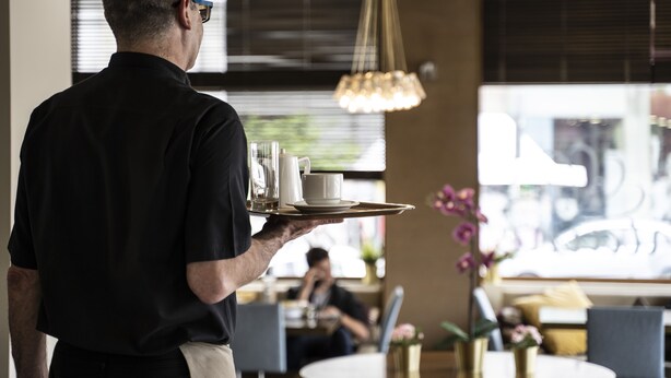 A waiter carrying a tray with a cup and saucer, a glass, and a pitcher. - Hotel Abc (Thessaloniki)