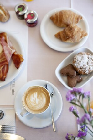 Mesa com croissants, bacon, biscoitos e uma xícara de café para o café da manhã.
