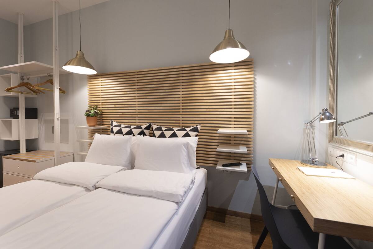 A modern bedroom with a bed, bedside tables, a desk, and a mirror.