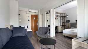 A modern hotel room with a bed, a sofa, a chair, a small table, and a wardrobe. - Hotel Abc (Thessaloniki)