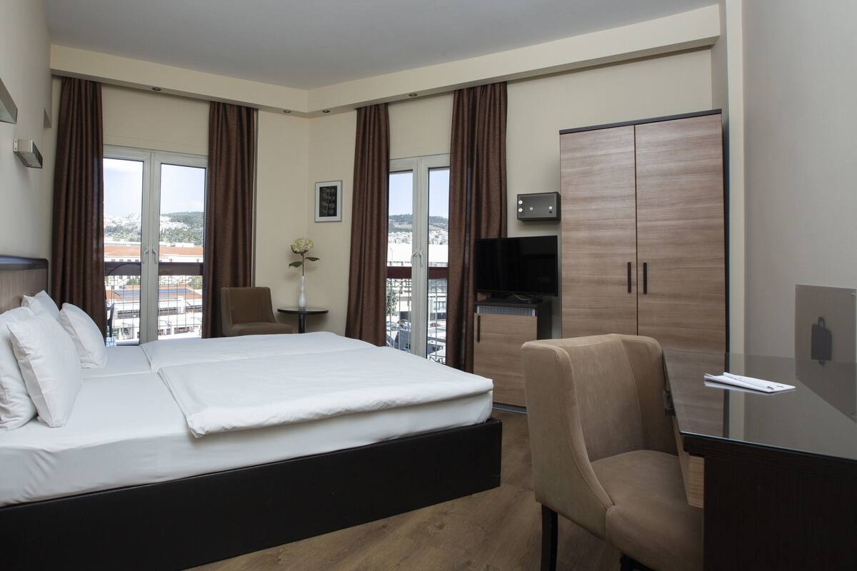 A hotel room with a bed, a desk, a chair, a TV, and a wardrobe.