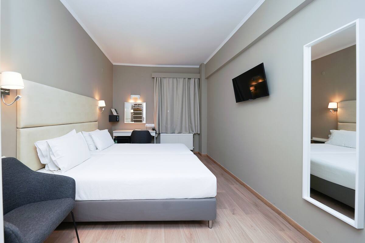 A hotel room with a bed, a desk, a chair, a TV, and a mirror.