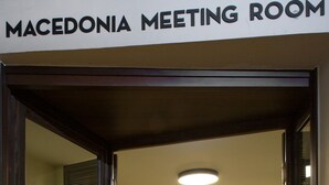 A meeting room with a sign reading "Macedonia Meeting Room," featuring a conference table surrounded by chairs, a tiled floor, and a modern ceiling light. - Hotel Abc (Thessaloniki)